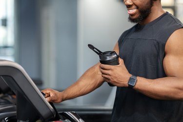 Close view of muscular person on treadmill holding bottle of krealkyline true athlete creatine shake