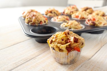 Tasty baked pizza muffins in a pan with one on the table
