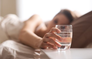 A person in bed reaching for a glass of water