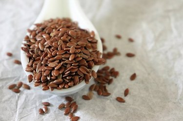 Close-up of omega-3-rich flax seeds in a ceramic spoon on white background
