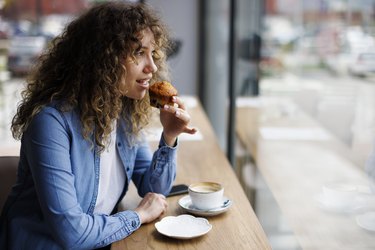 Young woman eating muffin and drinking coffee at a cafe